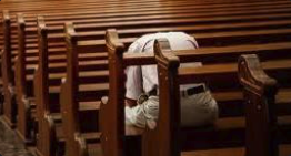 A lone worshipper in prayer in church pews